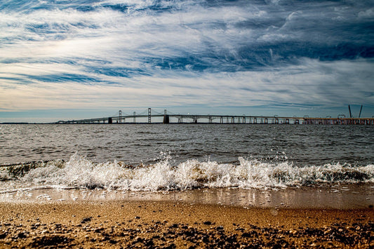Cinematic landscape of the Chesapeake Bay Bridge over water under a dramatic cloudy sky.