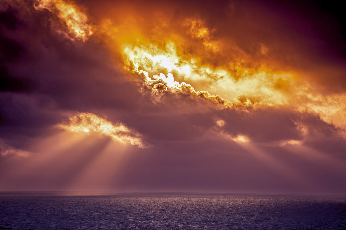 Dramatic sunset over the ocean with golden sunlight breaking through dark clouds