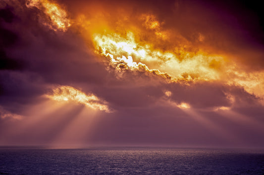 Dramatic sunset over the ocean with golden sunlight breaking through dark clouds