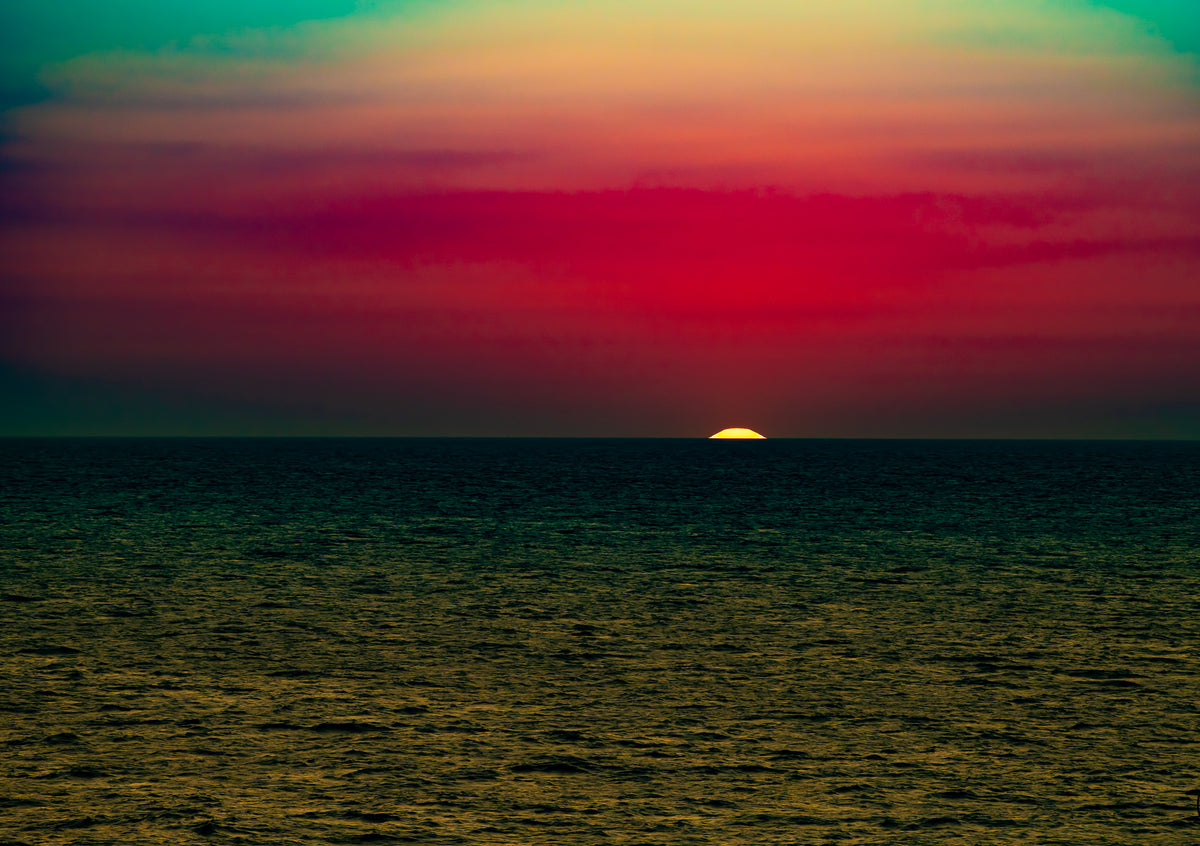 Cinematic sunset over a calm ocean with vibrant red and orange sky hues.