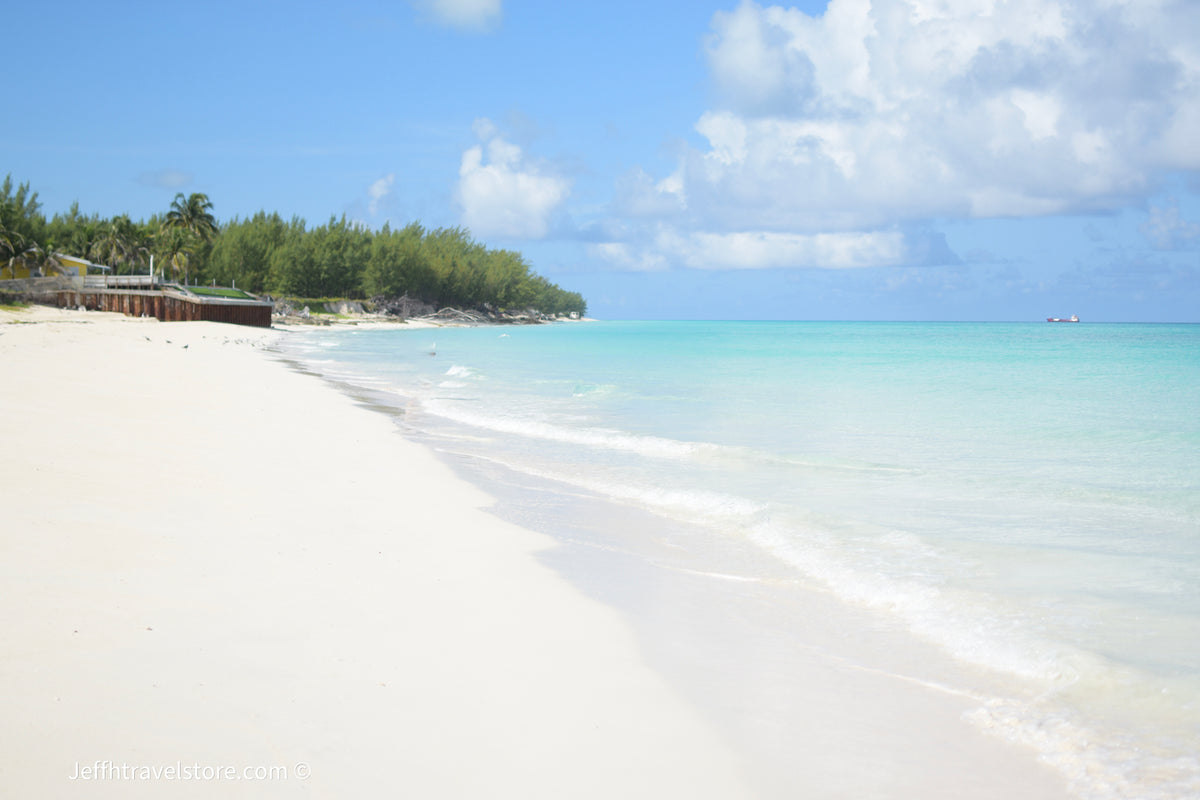 Cinematic view of a white sand beach with turquoise ocean waves under a cloudy blue sky.